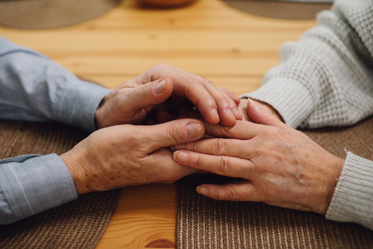 Two older hands clasped together over a wooden table